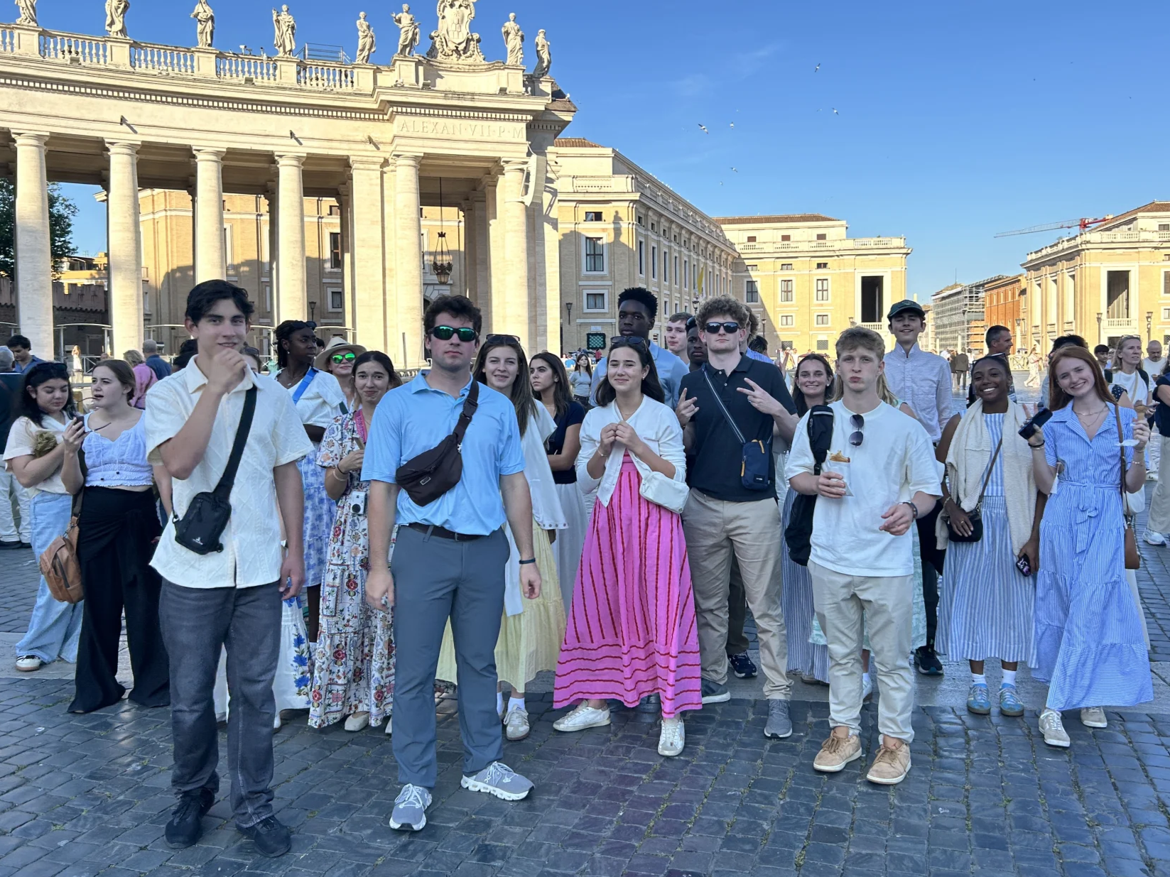 Group of young adults posing on a cobblestone plaza in front of the colonnade at St. Peter's Square, Vatican City