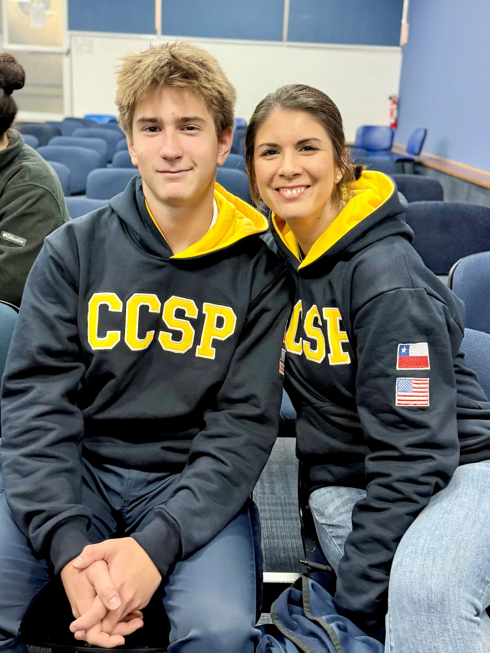Young man and woman seated in an auditorium, smiling and wearing matching black hoodies with yellow “CCSP” letters