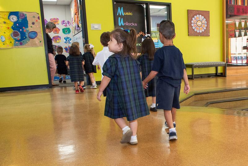 young boy and girl in school uniform holding hands walking in classroom